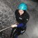 A woman, dressed in a wetsuit and helmet, rappels into a torrent of water